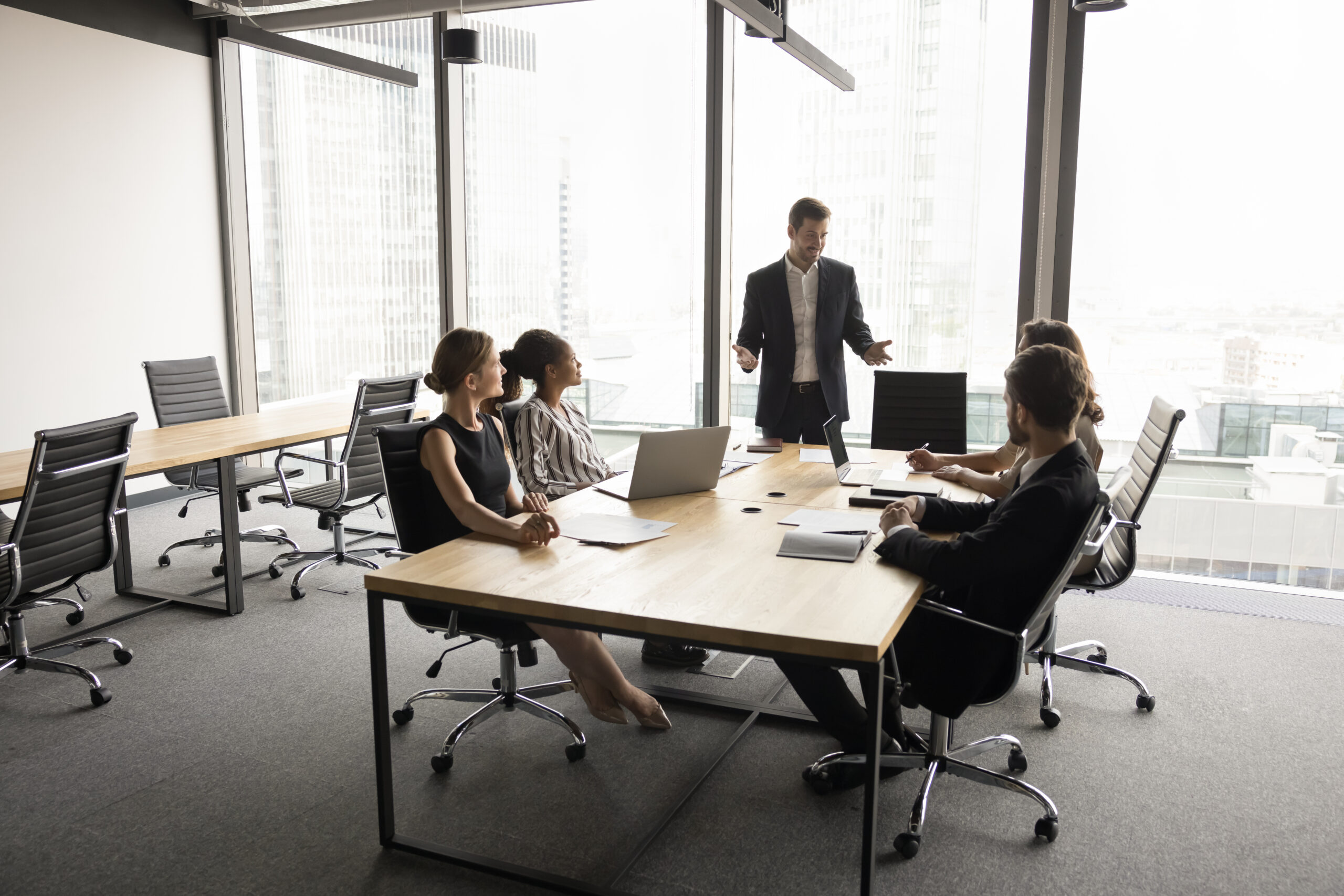 A business meeting in a modern conference room with a man presenting to a group of four colleagues seated at a large table.