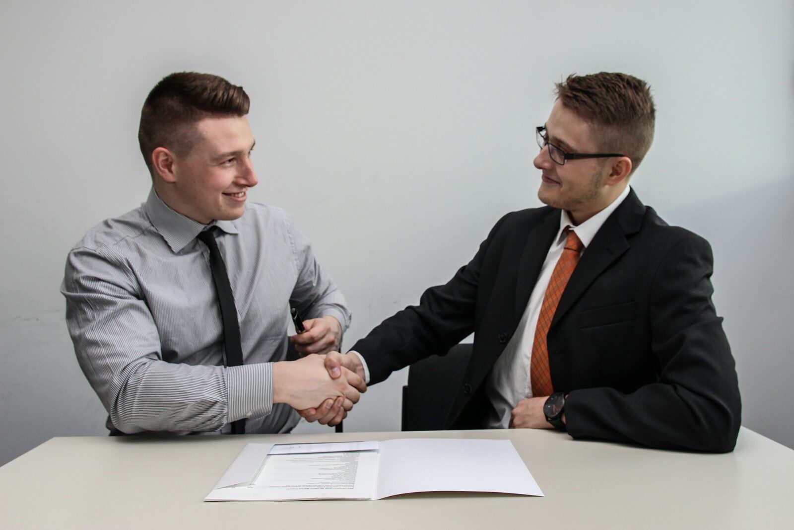 Two professionals shake hands over a table with a contract, signaling a successful business agreement in a formal setting.